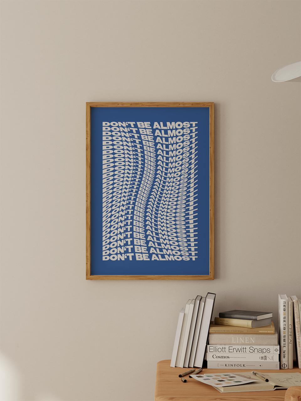 Poster „DON’T BE ALMOST“ in weißer dynamischer Wellenoptik auf blauem Hintergrund, gerahmt in Holz und dekorativ inszeniert im modernen Interieur - ALMOST A BRAND