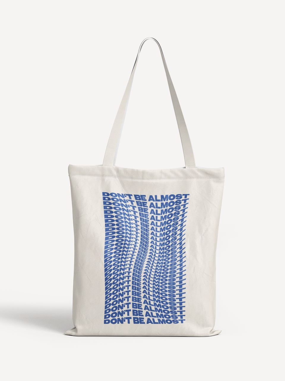 Beige Totebag mit wellenförmigem, blauem Schriftzug „DON’T BE ALMOST“ in Wiederholung – ALMOST A BRAND