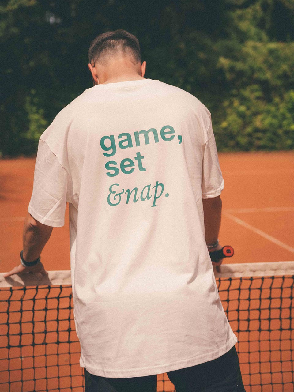 Männliches Modell trägt trägt das T-Shirt von Almost a Brand in Weiß mit grünem Rückendruck „game, set & nap.“