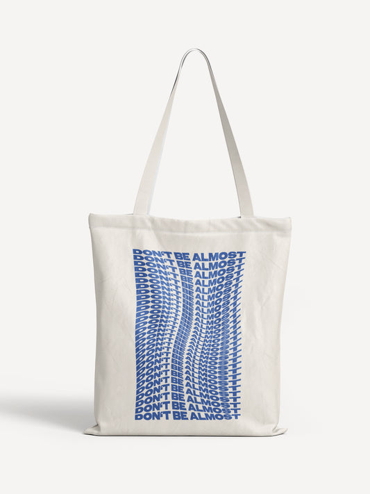 Beige Totebag mit wellenförmigem, blauem Schriftzug „DON’T BE ALMOST“ in Wiederholung – ALMOST A BRAND