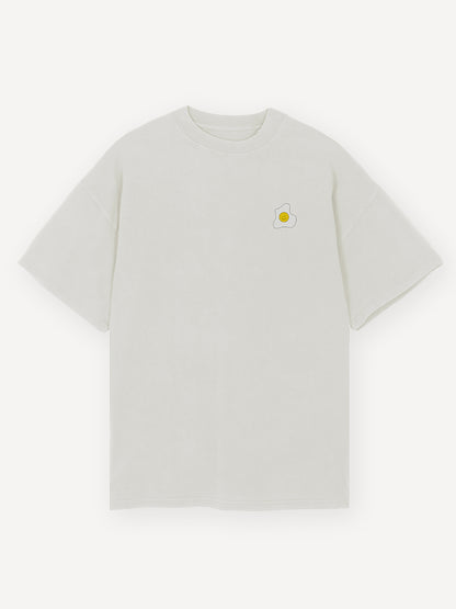 Ein kleines, minimalistisches Grafikmotiv eines lächelnden Spiegeleis befindet sich dezent auf der linken Brustseite auf einem weißen Oversized T-Shirt