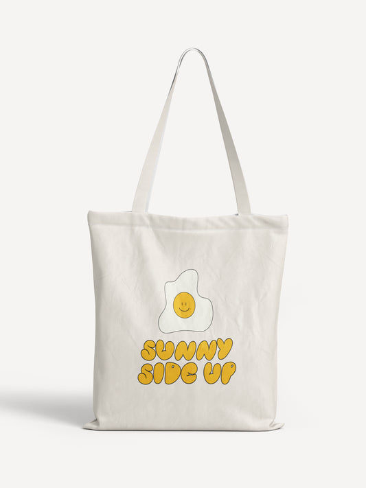 Weiße Stofftasche mit gelbem Aufdruck „SUNNY SIDE UP“ und einem lächelnden Spiegelei – verspieltes Design für gute Laune.