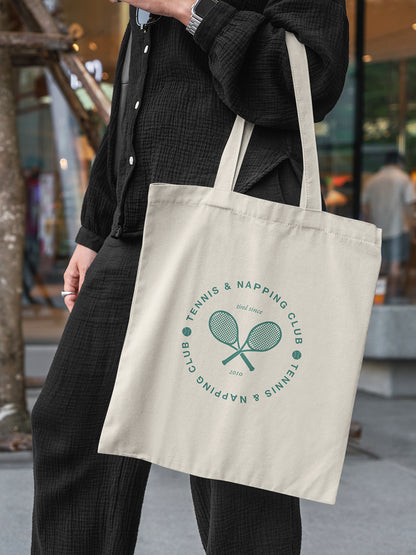 Frau trägt beigefarbene Totebag mit grünem Aufdruck „Tennis & Napping Club“ und zwei gekreuzten Tennisschlägern - ALMOST A BRAND